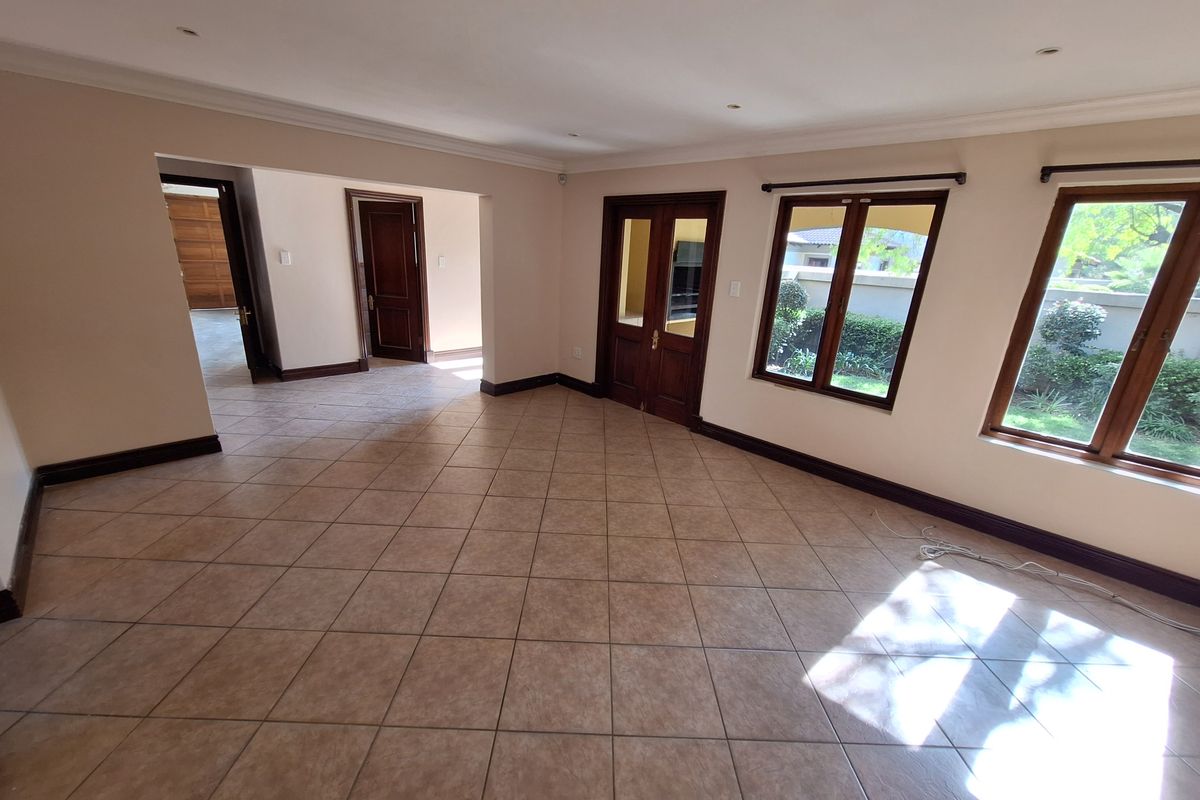 A spacious, empty living area featuring neutral walls, ceramic tiled flooring, and wooden door and window frames with natural light.