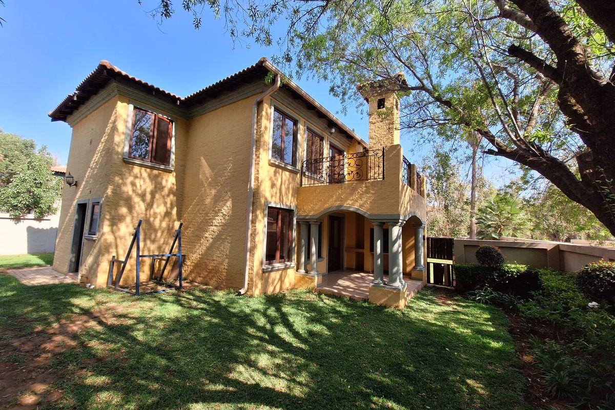 Rear view of a two-story house featuring a covered patio, upper balcony with wrought iron railing, and a landscaped garden area.