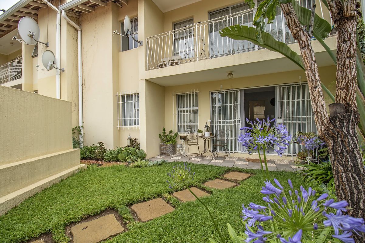 Rear view of the apartment featuring a small private garden, paved patio area, and balcony access with security bars on windows and doors.