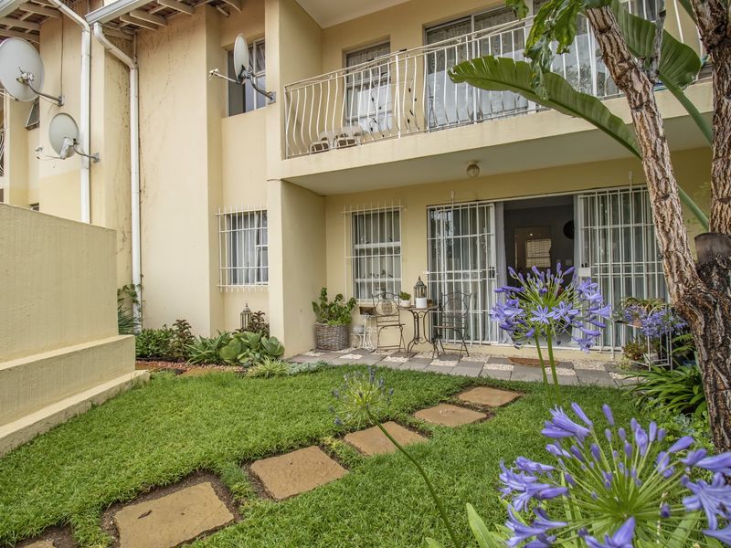 Rear view of the apartment featuring a small private garden, paved patio area, and balcony access with security bars on windows and doors.