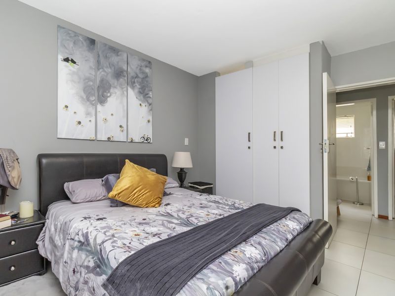 A well-maintained bedroom featuring neutral grey walls, built-in white cupboards, and tiled flooring, with an adjoining bathroom visible through the doorway.