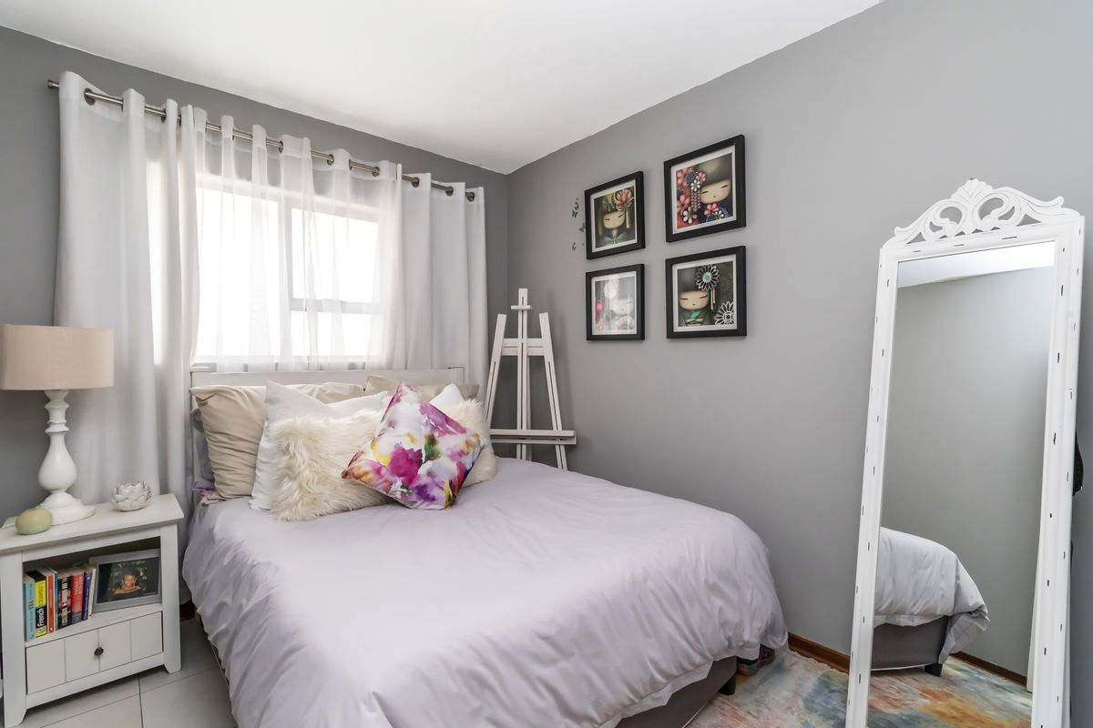 A well-maintained bedroom featuring neutral grey walls, tiled flooring, and a large window allowing for natural light.