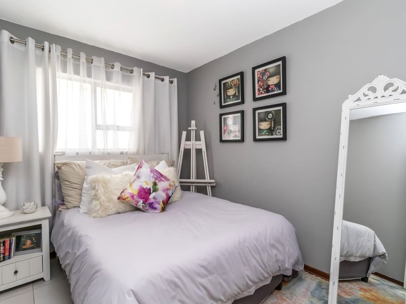 A well-maintained bedroom featuring neutral grey walls, tiled flooring, and a large window allowing for natural light.