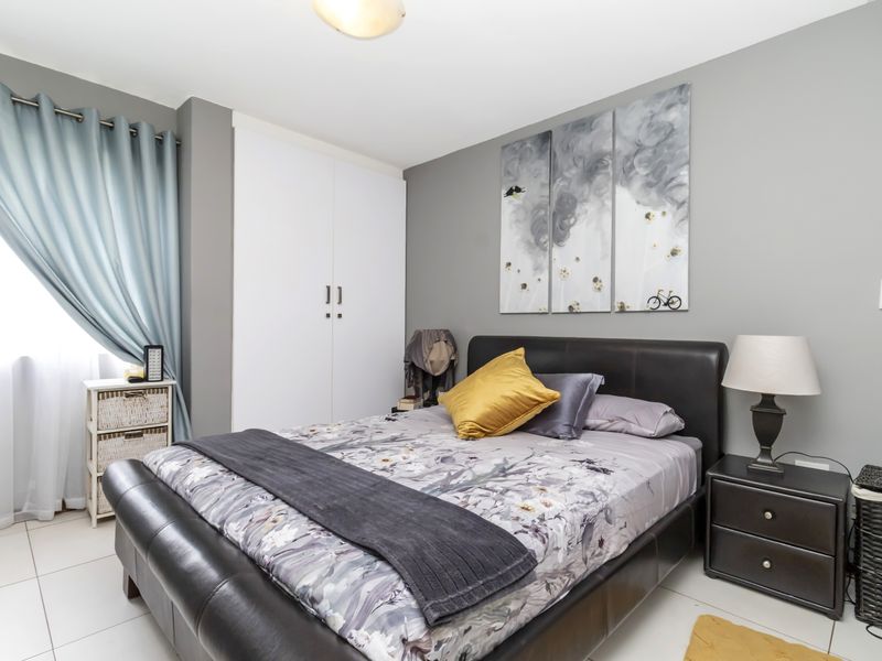 A well-maintained bedroom featuring neutral grey walls, tiled flooring, and a functional built-in wardrobe.