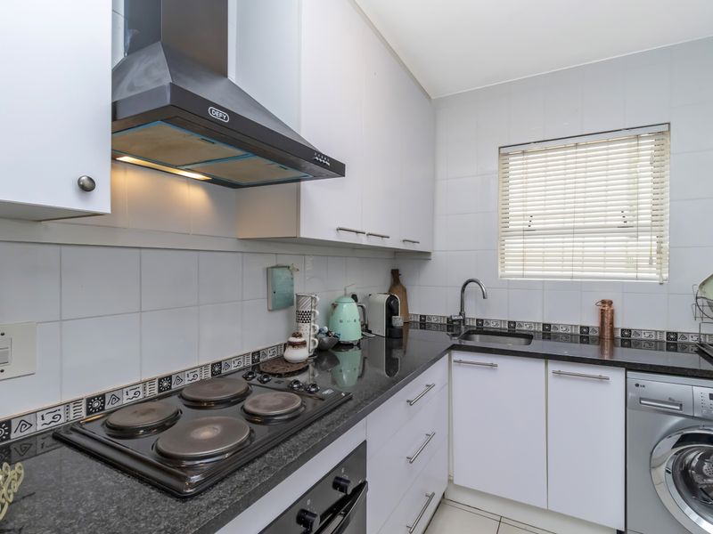 Compact kitchen featuring white cabinetry, dark granite countertops, a built-in electric hob, oven, extractor fan, and an integrated washing machine.