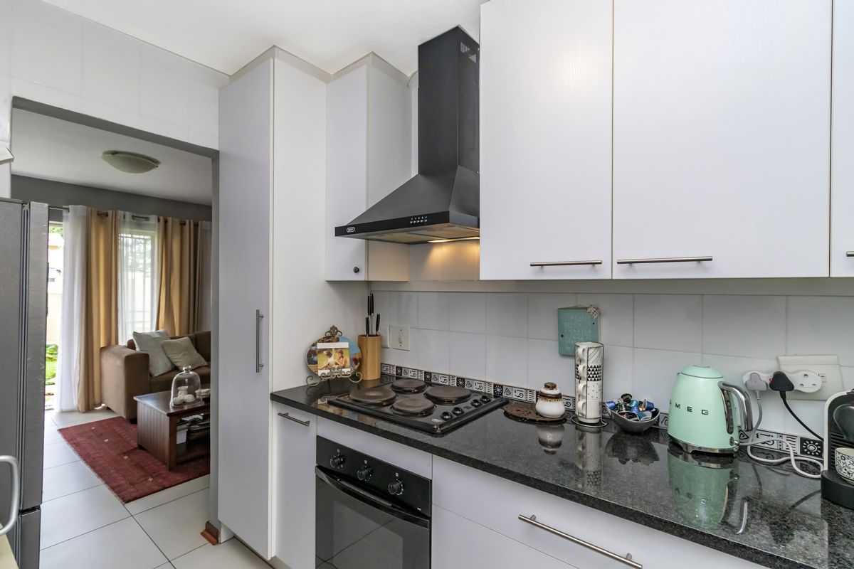 A functional kitchen featuring white cabinetry, granite countertops, a built-in oven, and an electric hob with an extractor fan.