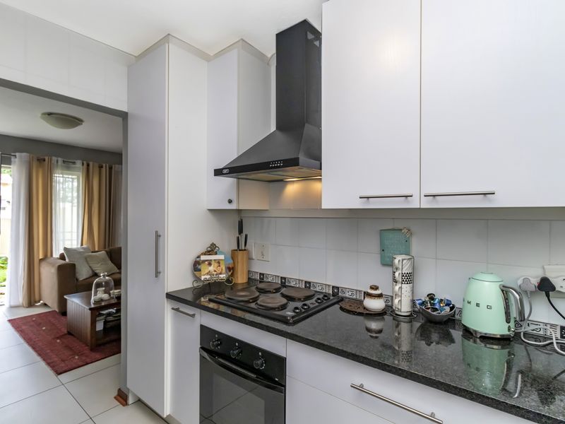A functional kitchen featuring white cabinetry, granite countertops, a built-in oven, and an electric hob with an extractor fan.