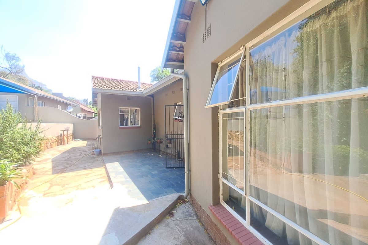Rear exterior view of the property featuring a paved patio area, stone walkway, and secure access gate with metal window frames.