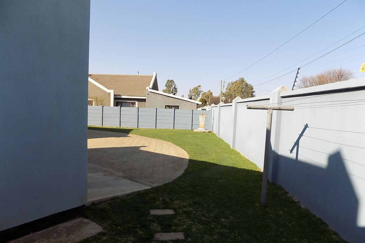 A private rear garden area featuring a paved section, well-maintained lawn, and secure precast concrete boundary walling.