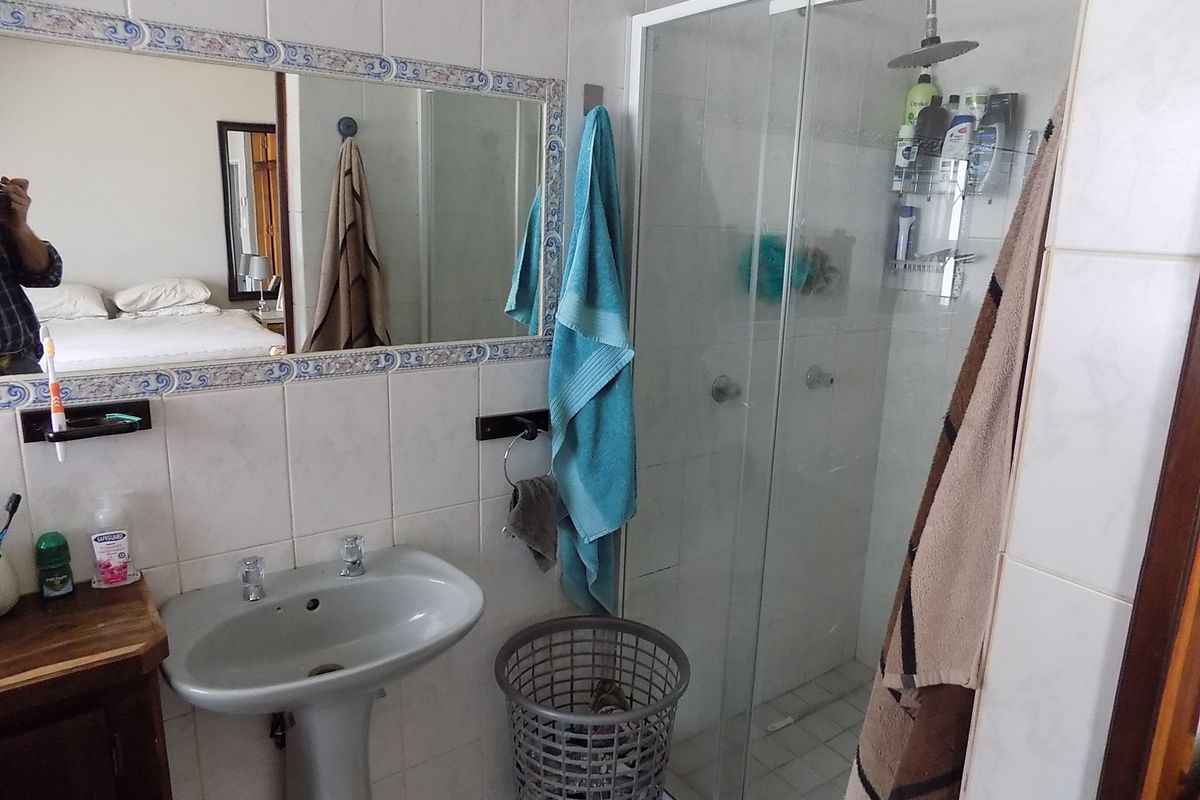 A functional bathroom featuring a pedestal basin, a glass-enclosed shower, and tiled wall finishes.