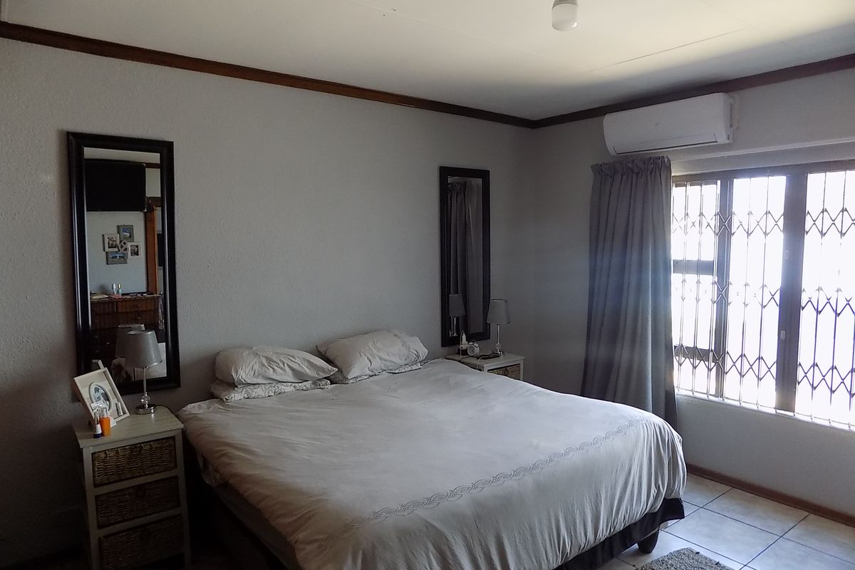 A functional bedroom featuring tiled flooring, a wall-mounted split-system air conditioner, and a window fitted with a security gate.