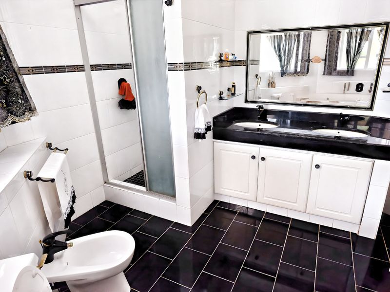 A functional bathroom featuring a double vanity with black granite countertop, a glass-enclosed shower, and a bidet, finished with high-contrast black and white tiling.