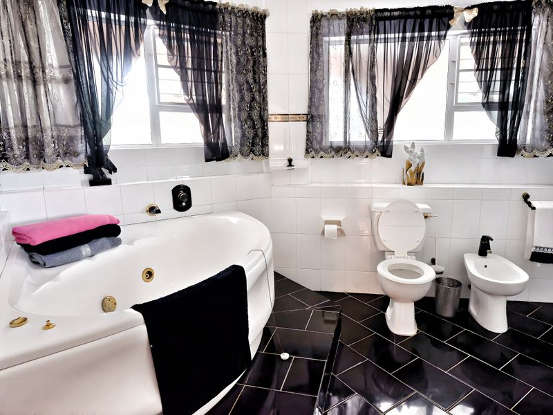 A spacious bathroom featuring a corner jetted bathtub, a white toilet, and a bidet, finished with high-contrast black and white tiling.