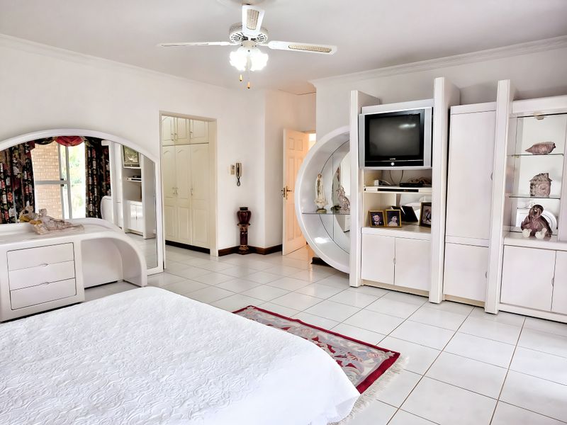 Spacious bedroom featuring white tiled flooring, built-in cabinetry, and a ceiling fan, offering a bright and functional living space.