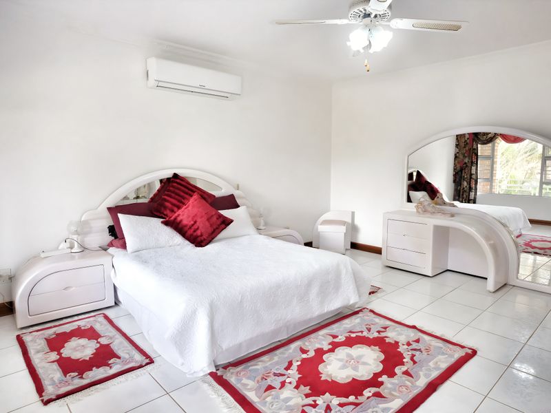 Spacious bedroom featuring white tiled flooring, a wall-mounted air conditioning unit, and a ceiling fan.