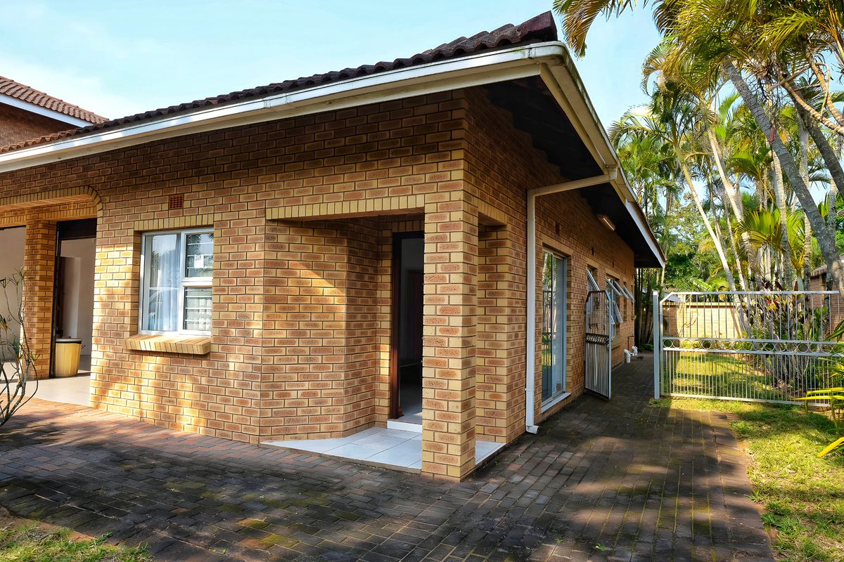 Exterior view of a face-brick house featuring a paved patio area, tiled entrance, and established garden surroundings.