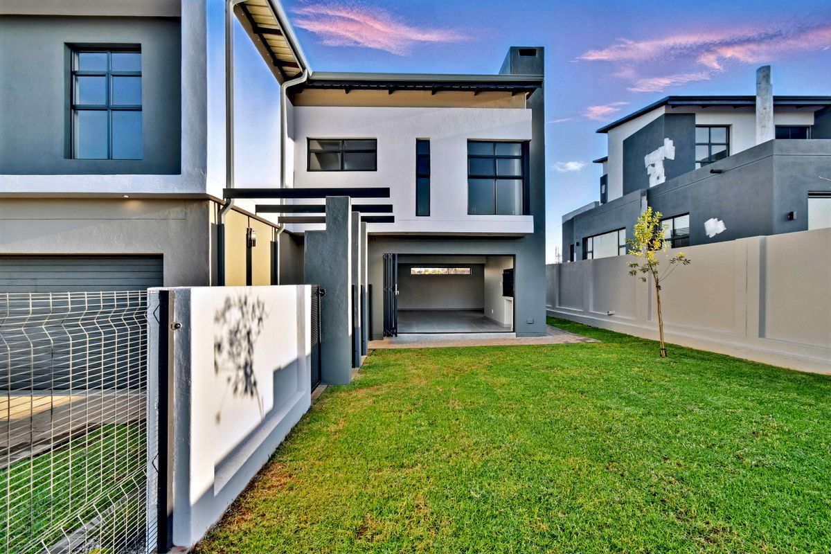 Rear view of a modern two-story home featuring a manicured lawn, paved patio area, and large bi-fold doors leading into the living space.