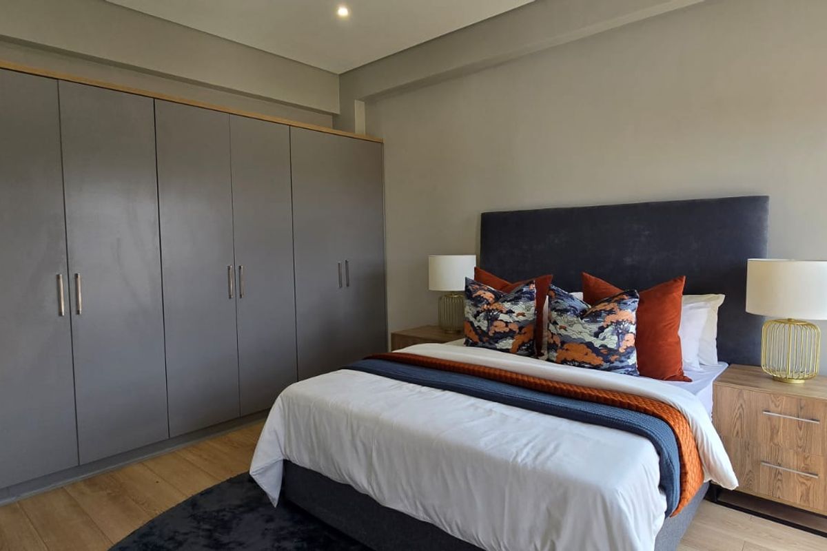 A modern bedroom featuring extensive built-in cupboards, neutral wall finishes, and light-toned laminate flooring.