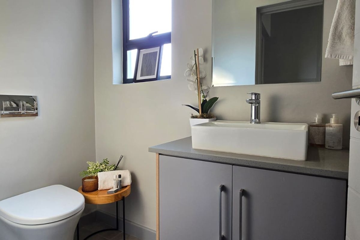 A modern bathroom featuring a wall-mounted toilet, a sleek vanity cabinet with a vessel sink, and a wall-mounted mirror.