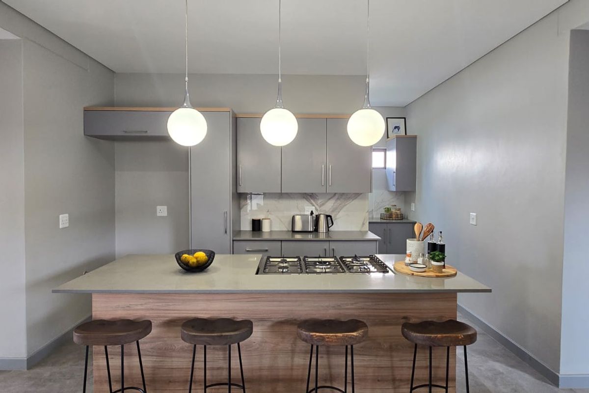 Modern kitchen featuring a central island with a built-in gas hob, sleek grey cabinetry, stone countertops, and contemporary pendant lighting.