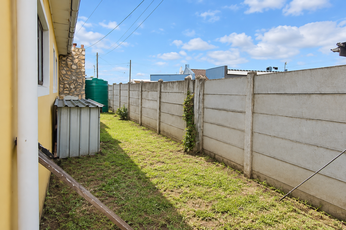 A side yard area featuring a precast concrete boundary wall, a water storage tank, and a small metal storage shed.