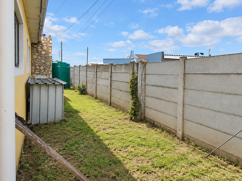 A side yard area featuring a precast concrete boundary wall, a water storage tank, and a small metal storage shed.