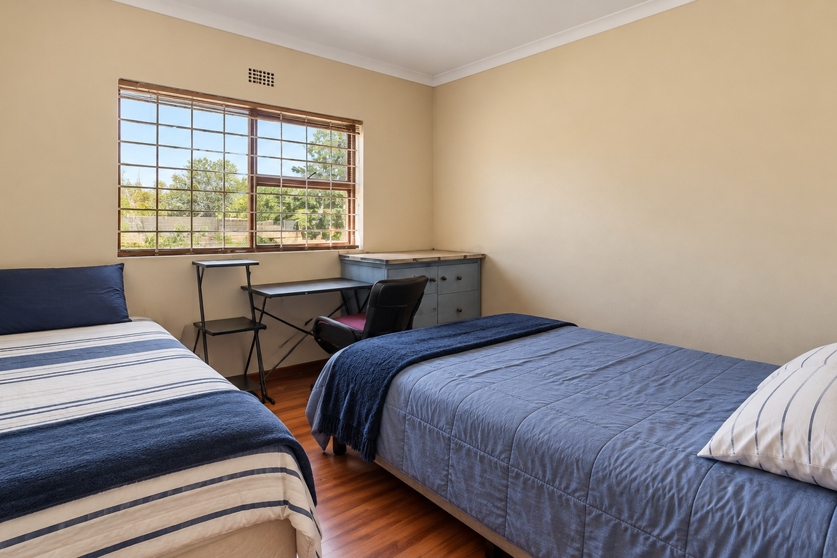A functional bedroom featuring laminate flooring, a window with security bars, and neutral wall finishes.