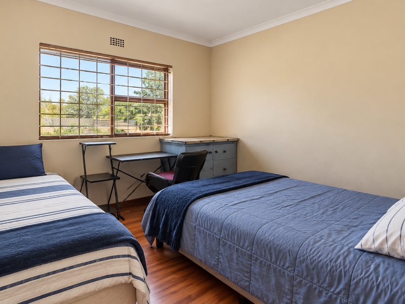 A functional bedroom featuring laminate flooring, a window with security bars, and neutral wall finishes.