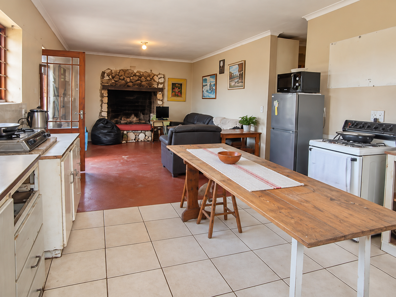 Open-plan living and kitchen area featuring a prominent stone fireplace, tiled flooring, and functional kitchen cabinetry in a dated, lived-in condition.
