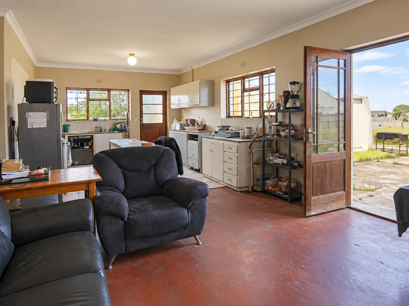 Open-plan kitchen and living area featuring built-in cabinetry, concrete flooring, and direct access to the rear garden through a timber-framed glass door.