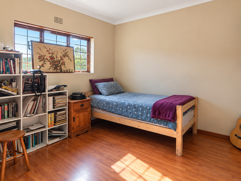 A functional bedroom featuring laminate flooring, security bars on the window, and built-in wall shelving.
