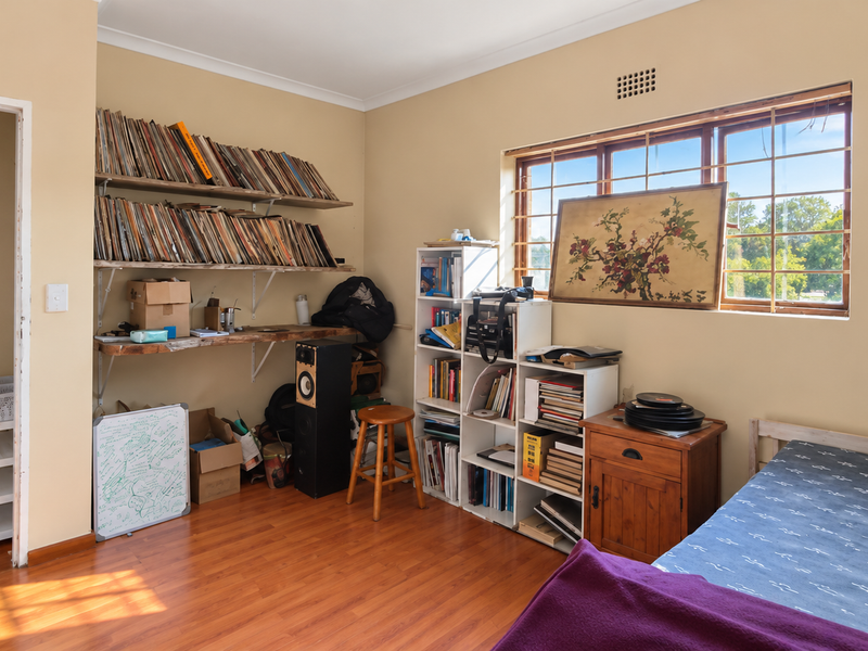 A bedroom featuring laminate flooring, built-in shelving, and a window fitted with security bars.