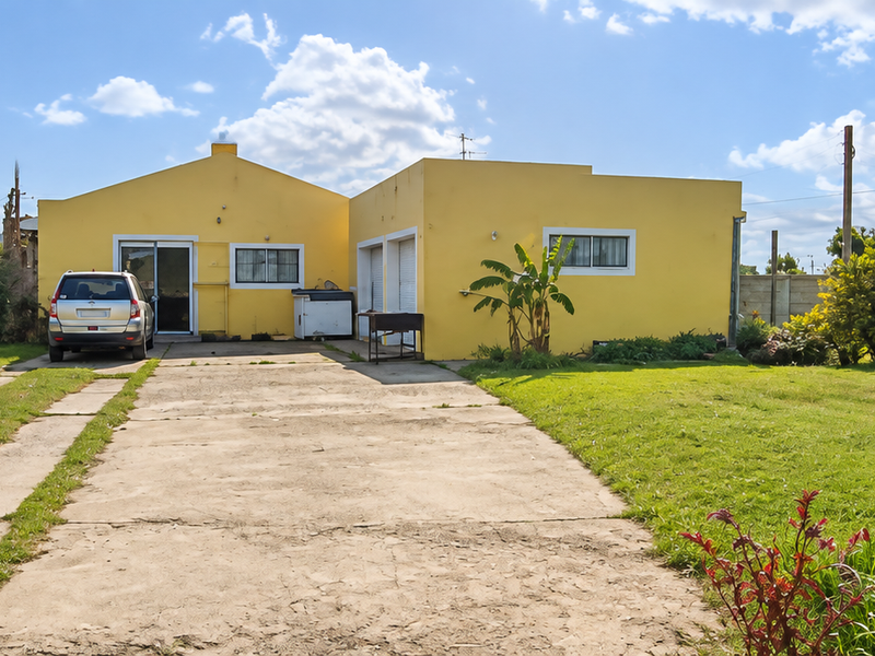 Rear view of a single-story yellow house featuring a concrete driveway, large lawn area, and precast boundary walling.