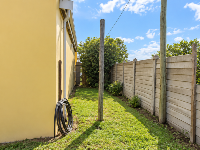A side garden area featuring a yellow exterior wall, a precast concrete boundary fence, and established greenery.