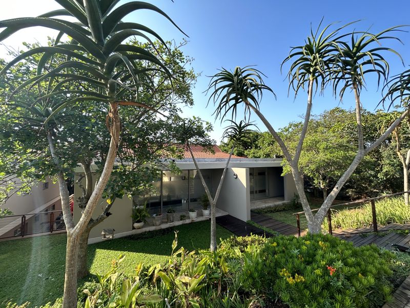 A well-maintained rear exterior view of the townhouse featuring a landscaped garden, timber decking, and large sliding glass doors leading to the interior.