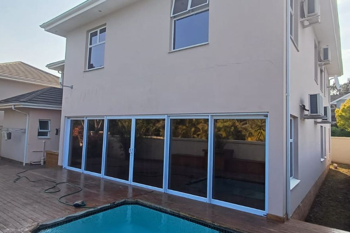 Rear exterior view of the house featuring a swimming pool, timber decking, and large sliding glass doors leading into the living area.