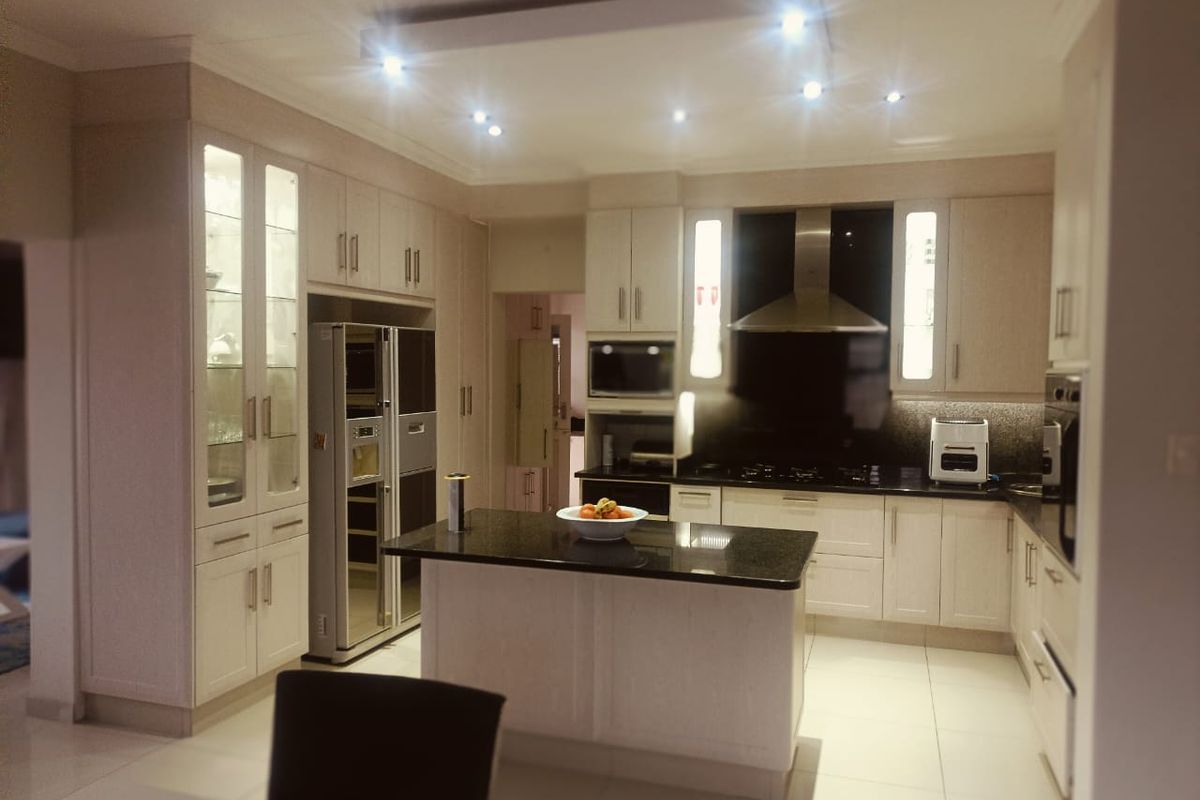 Modern kitchen featuring light-toned cabinetry, granite countertops, a central island, and integrated appliances with recessed ceiling lighting.