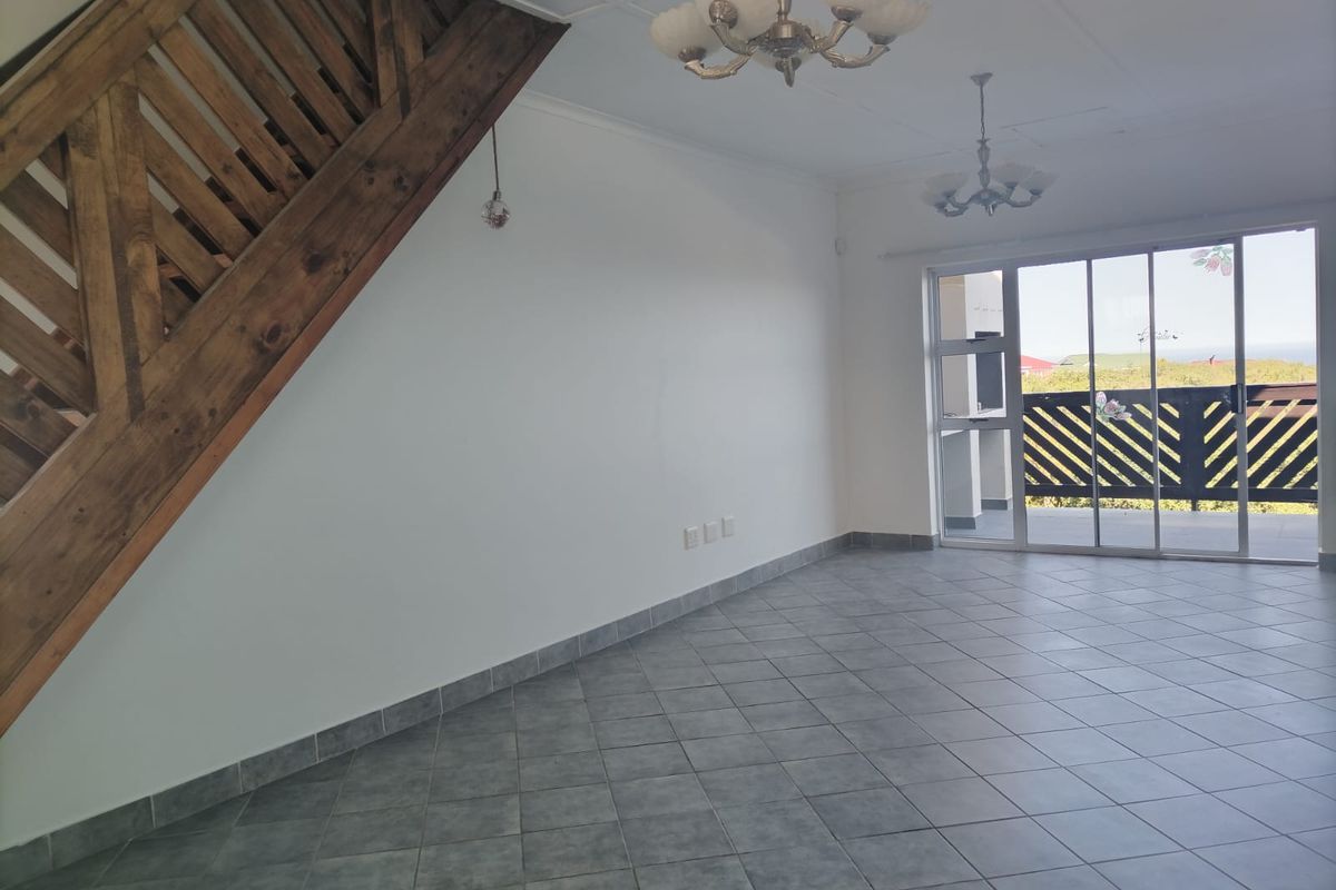 An open-plan living area featuring tiled flooring, a wooden staircase, and large sliding glass doors leading to an outdoor balcony.