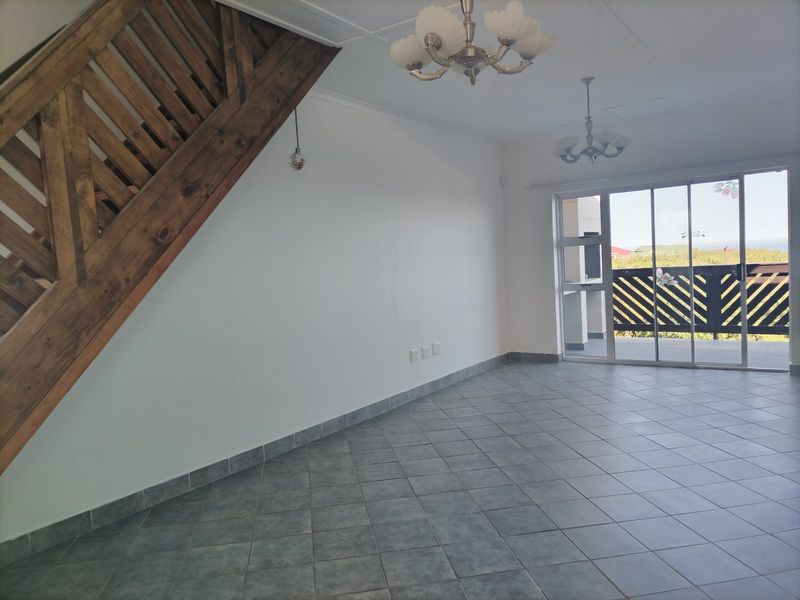 An open-plan living area featuring tiled flooring, a wooden staircase, and large sliding glass doors leading to an outdoor balcony.