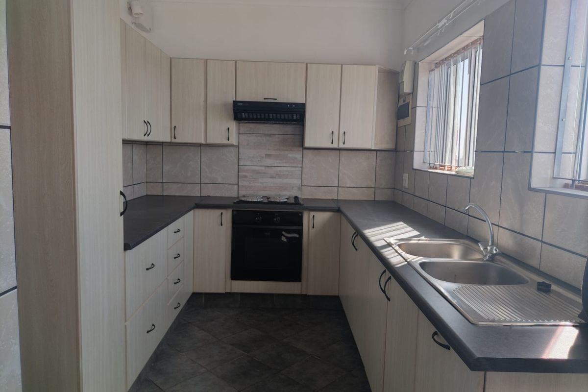 A functional kitchen featuring light-toned built-in cabinetry, dark laminate countertops, a double stainless steel sink, and integrated oven with extractor fan.