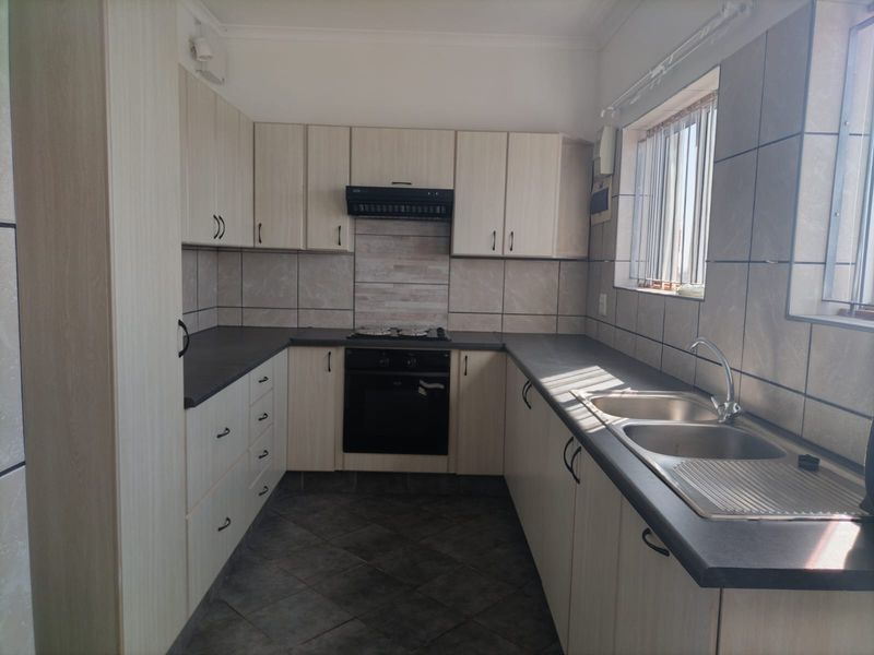 A functional kitchen featuring light-toned built-in cabinetry, dark laminate countertops, a double stainless steel sink, and integrated oven with extractor fan.