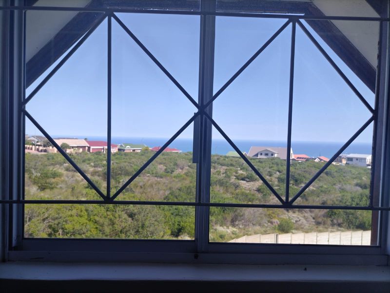 A view of the coastal landscape and ocean seen through a window with fixed security bars.