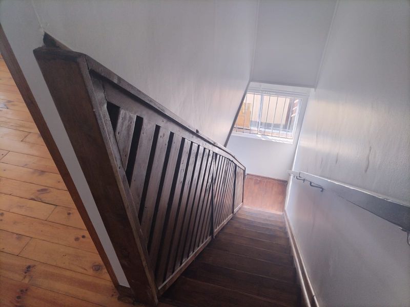 A functional staircase featuring timber flooring, a wooden balustrade, and a metal handrail, leading to a landing with a security-barred window.