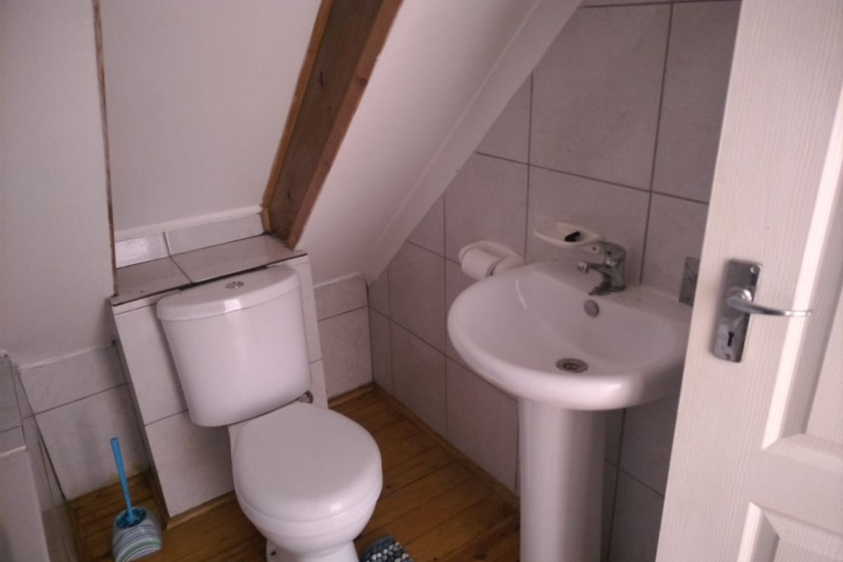 Compact bathroom featuring a pedestal basin, toilet, tiled walls, and exposed timber beam detail under a sloped ceiling.