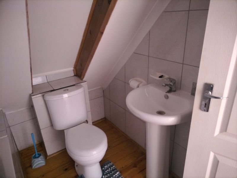 Compact bathroom featuring a pedestal basin, toilet, tiled walls, and exposed timber beam detail under a sloped ceiling.