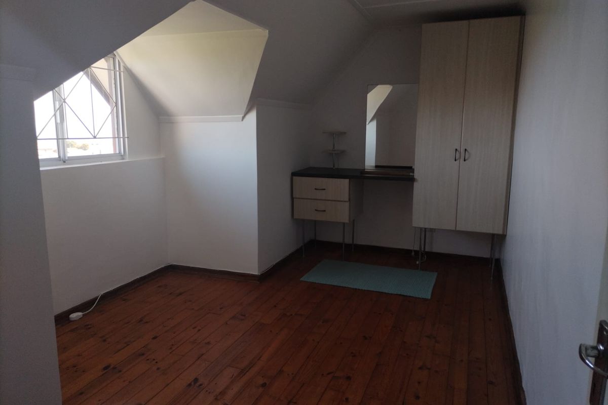 A bedroom featuring timber flooring, a dormer window with security bars, and built-in cabinetry including a wardrobe and vanity unit.