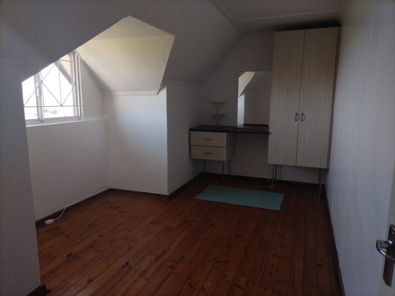 A bedroom featuring timber flooring, a dormer window with security bars, and built-in cabinetry including a wardrobe and vanity unit.