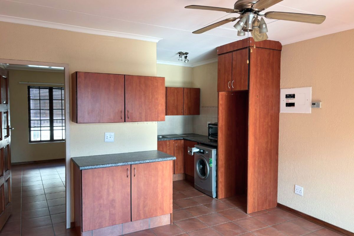 A functional kitchen area featuring laminate cabinetry, tiled flooring, and a ceiling fan, offering a practical layout for daily use.