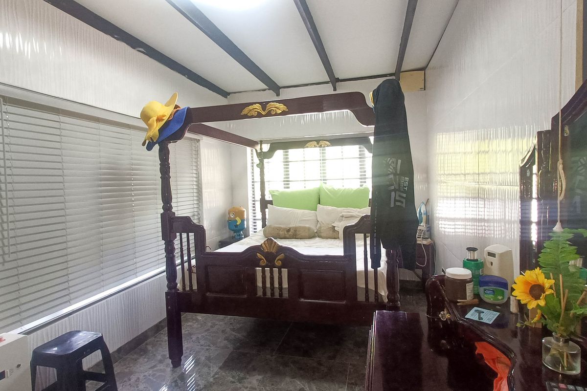 A bedroom featuring tiled flooring, wall cladding, and large windows with blinds, providing a functional sleeping space.