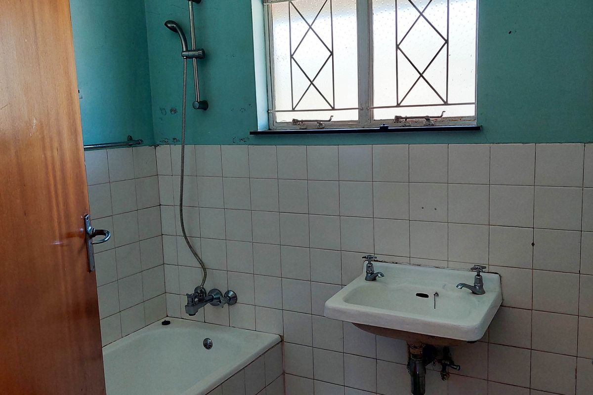 A dated bathroom featuring a built-in bathtub with shower attachment, wall-mounted basin, and tiled finishes in need of modernization.